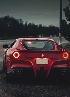 the rear end of a red sports car parked on the side of the road at night