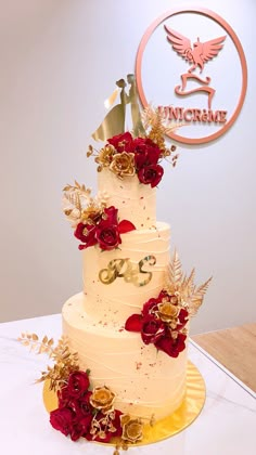 a three tiered wedding cake with red flowers and gold leaves on the bottom layer