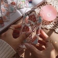 a woman is holding up her phone case in front of an open book on the table