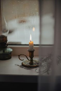 a lit candle sitting on top of a table next to a glass window sill