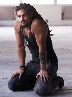 a man with long hair and tattoos on his arm crouching down to pose for the camera