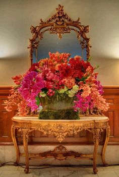 a vase filled with pink and red flowers sitting on top of a table next to a mirror