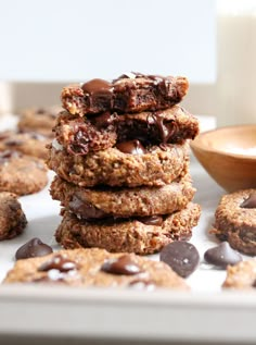 chocolate chip cookies stacked on top of each other next to a bowl of milk and a wooden spoon