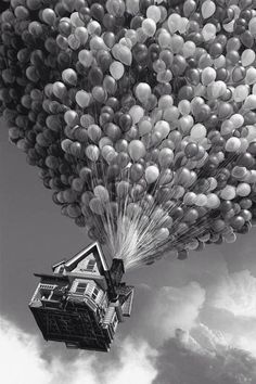 a bunch of balloons floating in the air over a house and clouds with a sky background