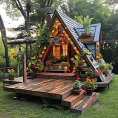 a small wooden house with plants and potted plants on the front porch is lit up by string lights