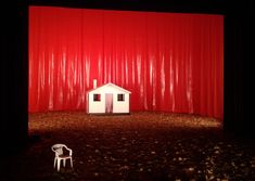 a small white chair sitting in front of a red curtain on top of a stage