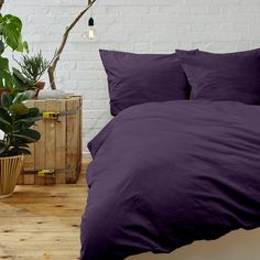 a bed with purple sheets and pillows in a room next to a potted plant