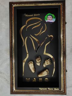 a shadow frame with baby's feet and footprints in gold foil on a white wall