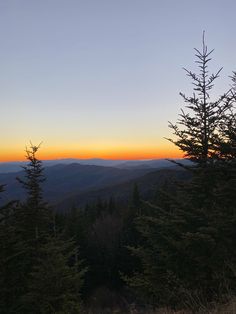 the sun is setting over some trees in the mountains