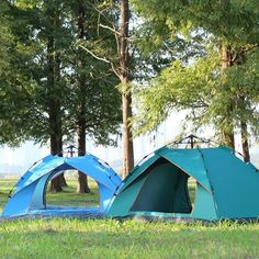 two blue tents sitting in the grass near trees