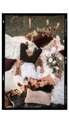 two people are laying on the ground with flowers and candles in their hands, one person is kissing the woman's head