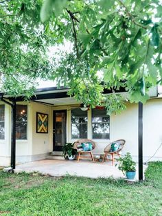 a small white house with two chairs on the front porch and green grass around it