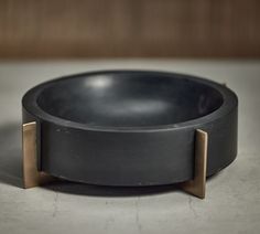 a black bowl with two gold handles on the bottom, sitting on a gray surface