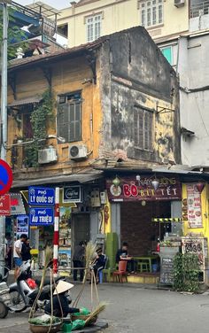 an old building in the middle of a street with people sitting on it and walking around