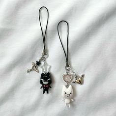 two key chains with charms attached to them on a white sheeted surface, one has a black cat and the other has a pink heart