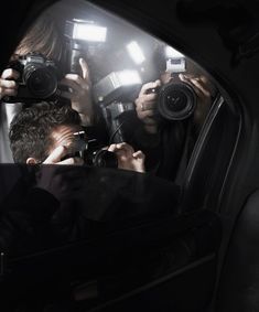 two people taking pictures in the side mirror of a car while another person holds up their camera