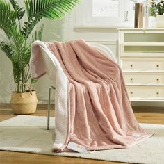 a pink blanket sitting on top of a white chair next to a potted plant