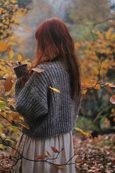 a woman is standing in the leaves with her back to the camera