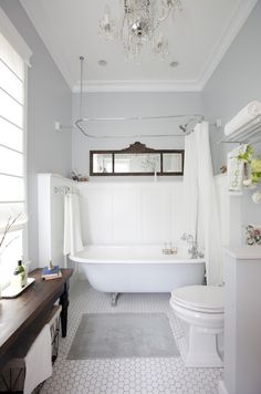 a white bath tub sitting under a chandelier next to a toilet and sink