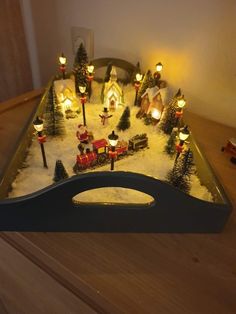 a lighted christmas village is displayed on a table with candles and trees in the snow