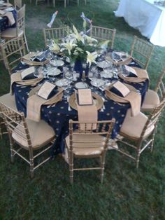 a table set up with blue and white linens for an outdoor wedding reception in the grass