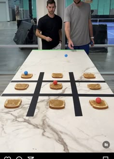 two men standing next to a table with cookies on it