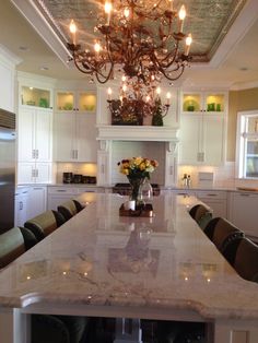 a chandelier hangs from the ceiling above a large kitchen island with marble counter tops