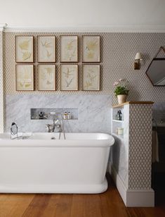 a white bath tub sitting in a bathroom next to a wall with pictures on it