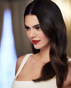 a woman with long dark hair wearing a white dress and red lipstick on her lips