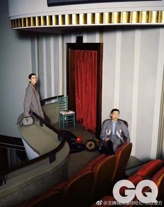 two men are sitting on chairs in a room with striped walls and red drapes