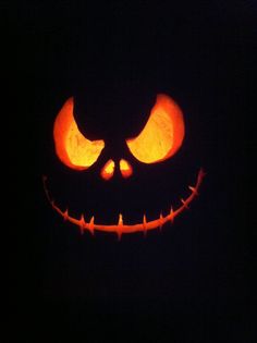 a carved jack o lantern in the dark with its eyes glowing orange and smiling at the camera