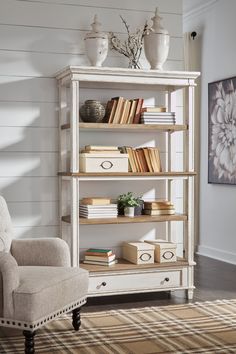 a white book shelf filled with lots of books next to a chair and rug in a room