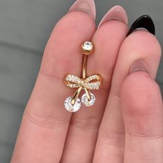 a woman's hand holding a gold nose ring with two clear stones on it