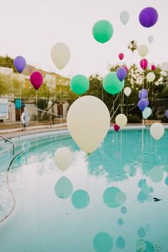 many balloons floating in the air near a swimming pool