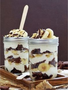 two mason jars filled with desserts on top of a wooden tray and topped with banana slices