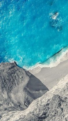 an aerial view of the ocean and beach from high up on a mountain side, with blue water in the background