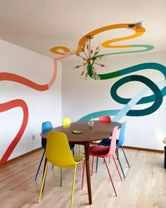 a dining room table with colorful chairs and a chandelier hanging from the ceiling