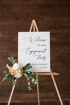 a sign with flowers and greenery on it sitting in front of a wooden wall