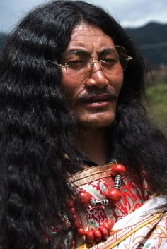 a man with long black hair wearing glasses and a red beaded headdress