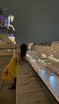 a woman leaning on a ledge looking at the city lights and traffic in the distance