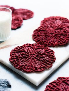 three red coasters sitting on top of a white plate next to a glass of milk