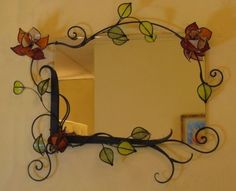 a mirror that is on the wall with vines and flowers painted on it's sides