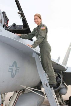 a woman in an air force uniform standing on the wing of a fighter jet plane