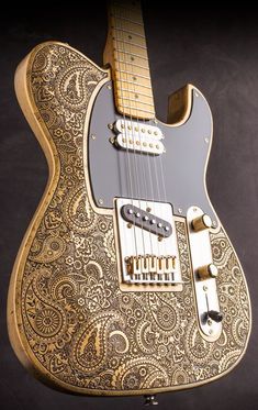 an intricately designed guitar is shown in this image, with gold and black paisley on it