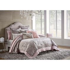 a bed covered in pink and grey comforter next to a window with chandelier