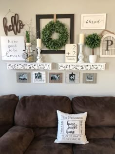 a brown couch sitting in front of a wall filled with pictures and framed wreaths