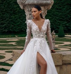 a woman in a white wedding dress standing next to a fountain with her legs crossed