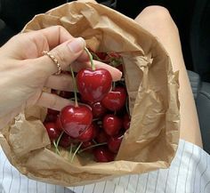 a person holding a paper bag full of cherries in their hand and sitting down