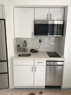 an empty kitchen with white cabinets and stainless steel dishwasher, refrigerator and microwave