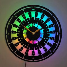 a black clock with multicolored numbers on it's face is shown in the dark